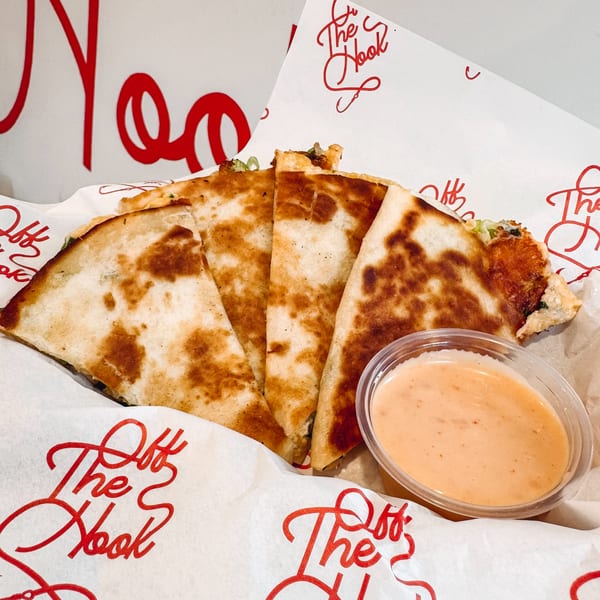 Four quesadilla slices with a side of dipping sauce, served in branded Off The Hook paper.